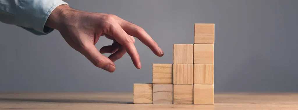 Close-up photo: Man's hand stacking wooden blocks, forming stairs on pink paper. Business growth, success process, copy space.